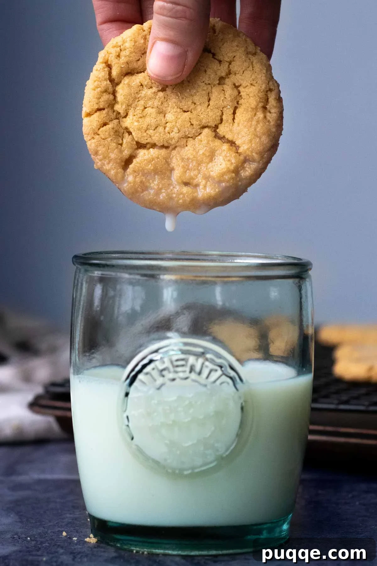 A perfectly baked, soft almond flour peanut butter cookie being dipped into a cold glass of milk, emphasizing its chewy texture and classic appeal.