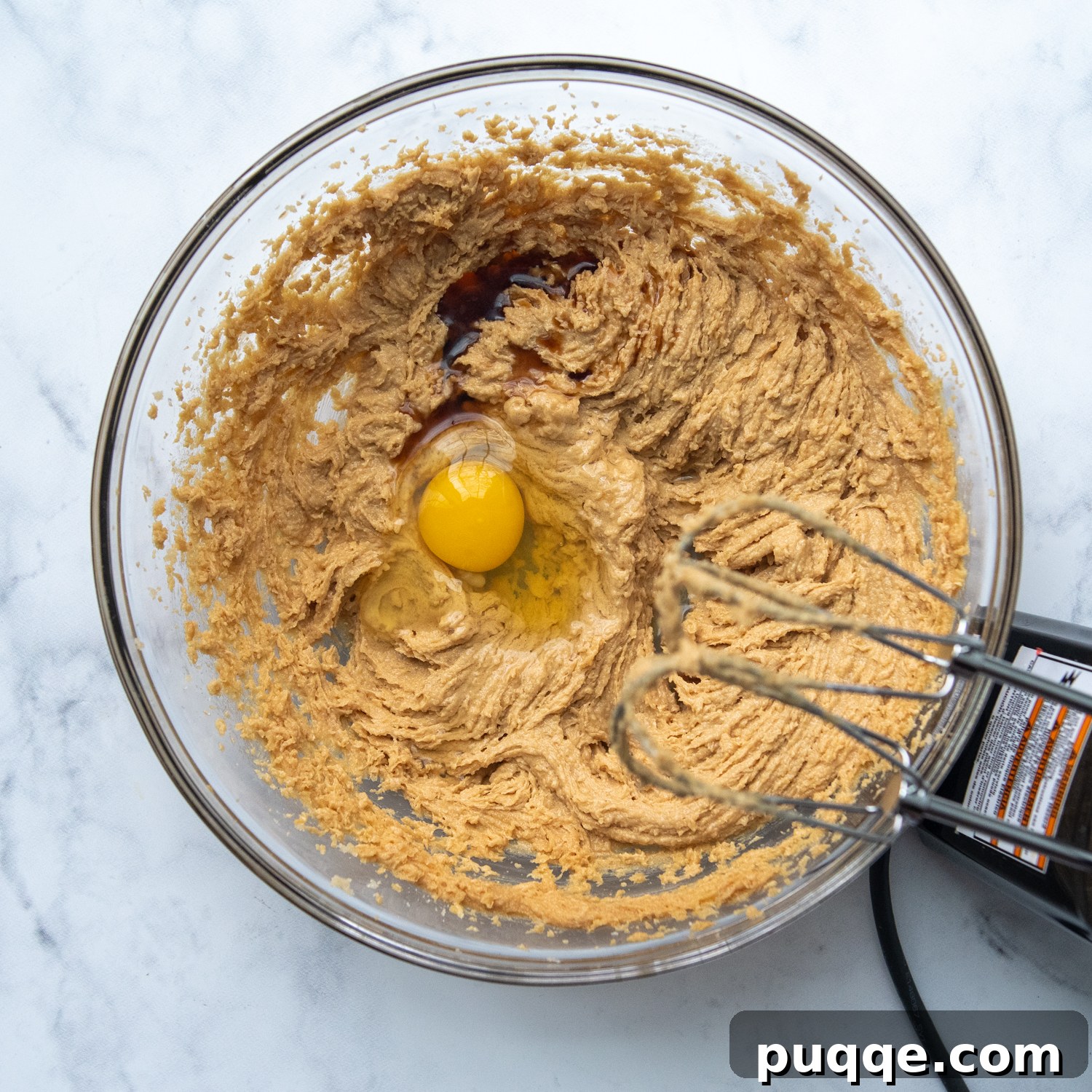 The perfectly creamy and combined peanut butter cookie dough with a single egg just cracked into the mixing bowl, ready to be incorporated.