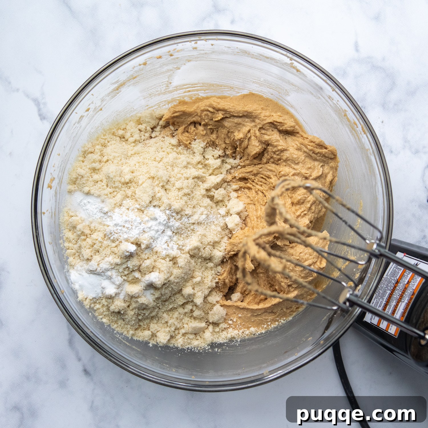 Blanched almond flour being gently mixed into the wet ingredients in a mixing bowl, illustrating the final stage of dough preparation.