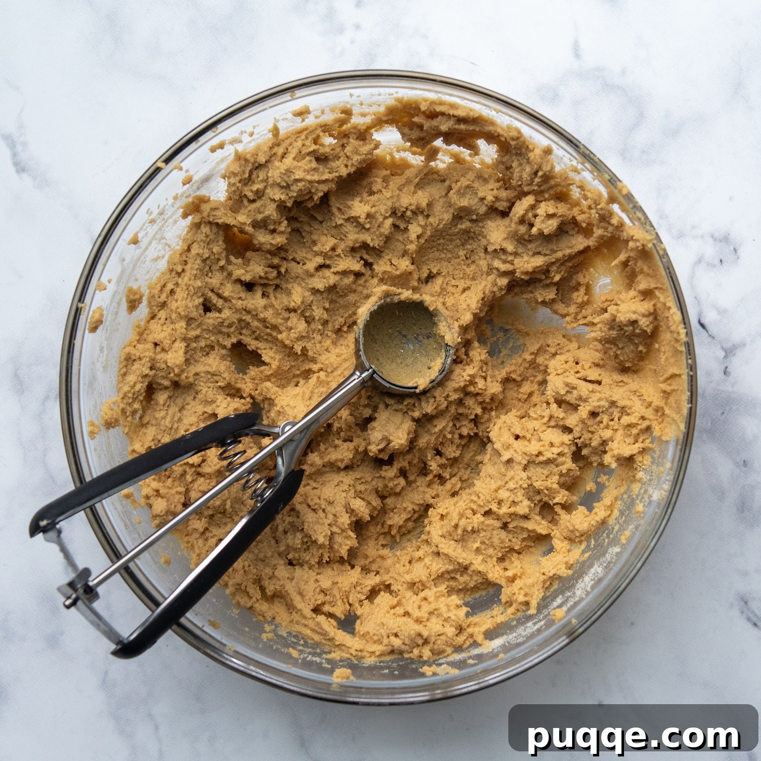 A small cookie scoop perfectly portioning out the soft peanut butter cookie dough from the bowl, demonstrating the ease of preparation.