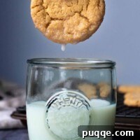 A soft almond flour peanut butter cookie caught mid-dunk into a tall glass of fresh milk, highlighting its perfect texture and classic pairing.