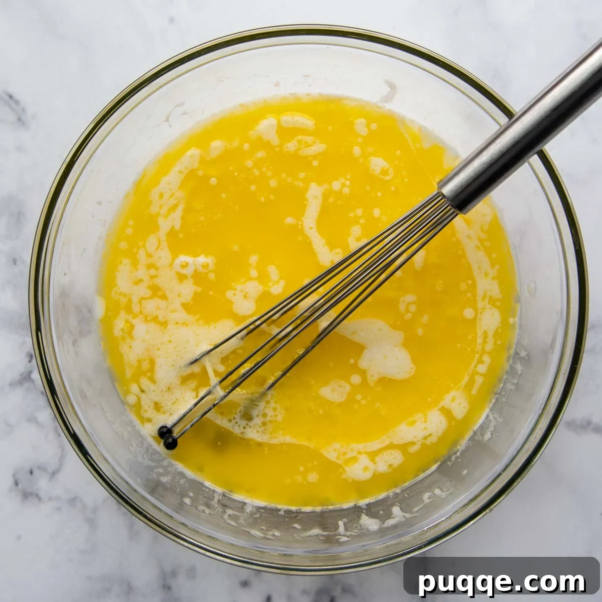 Wet ingredients including cooled melted butter, milk, egg whites, and vanilla extract whisked together in a clear glass bowl.
