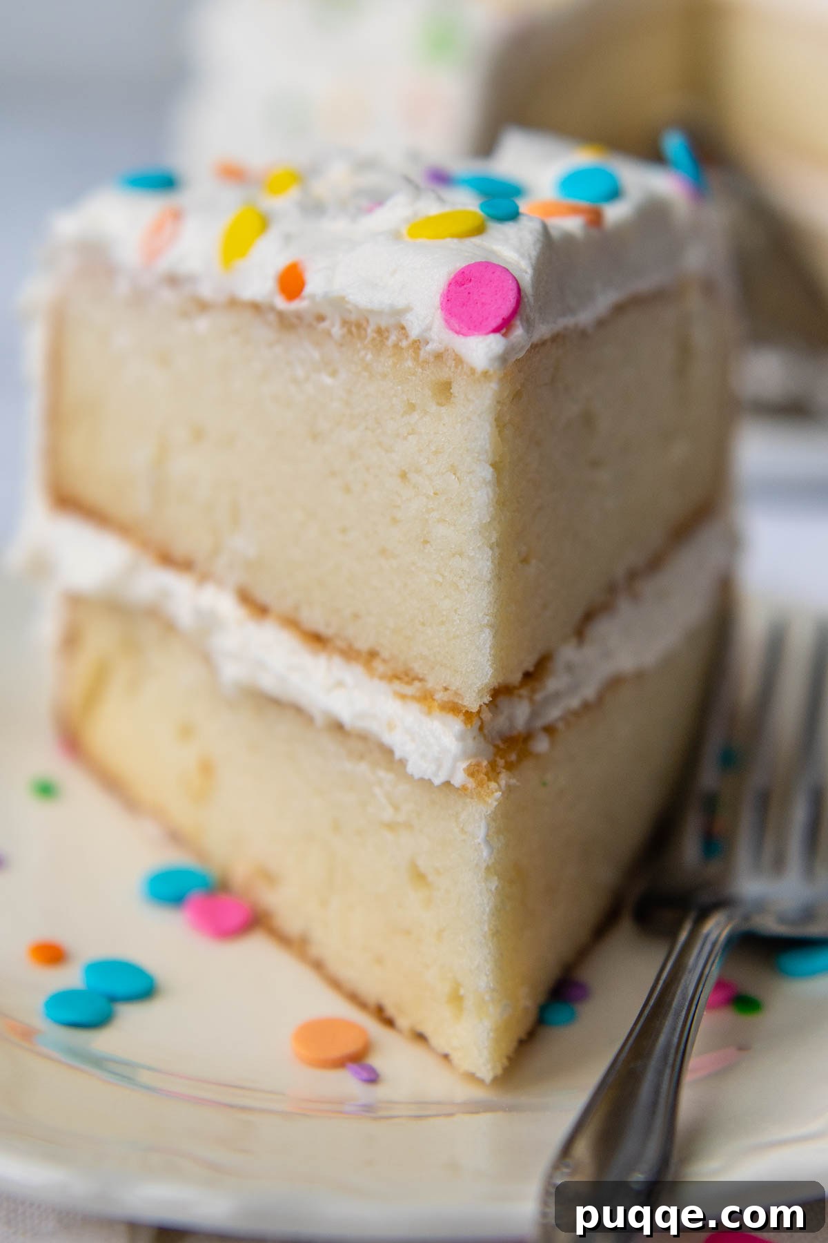 A perfectly frosted slice of fluffy gluten-free white cake on a plate, showing its moist interior.