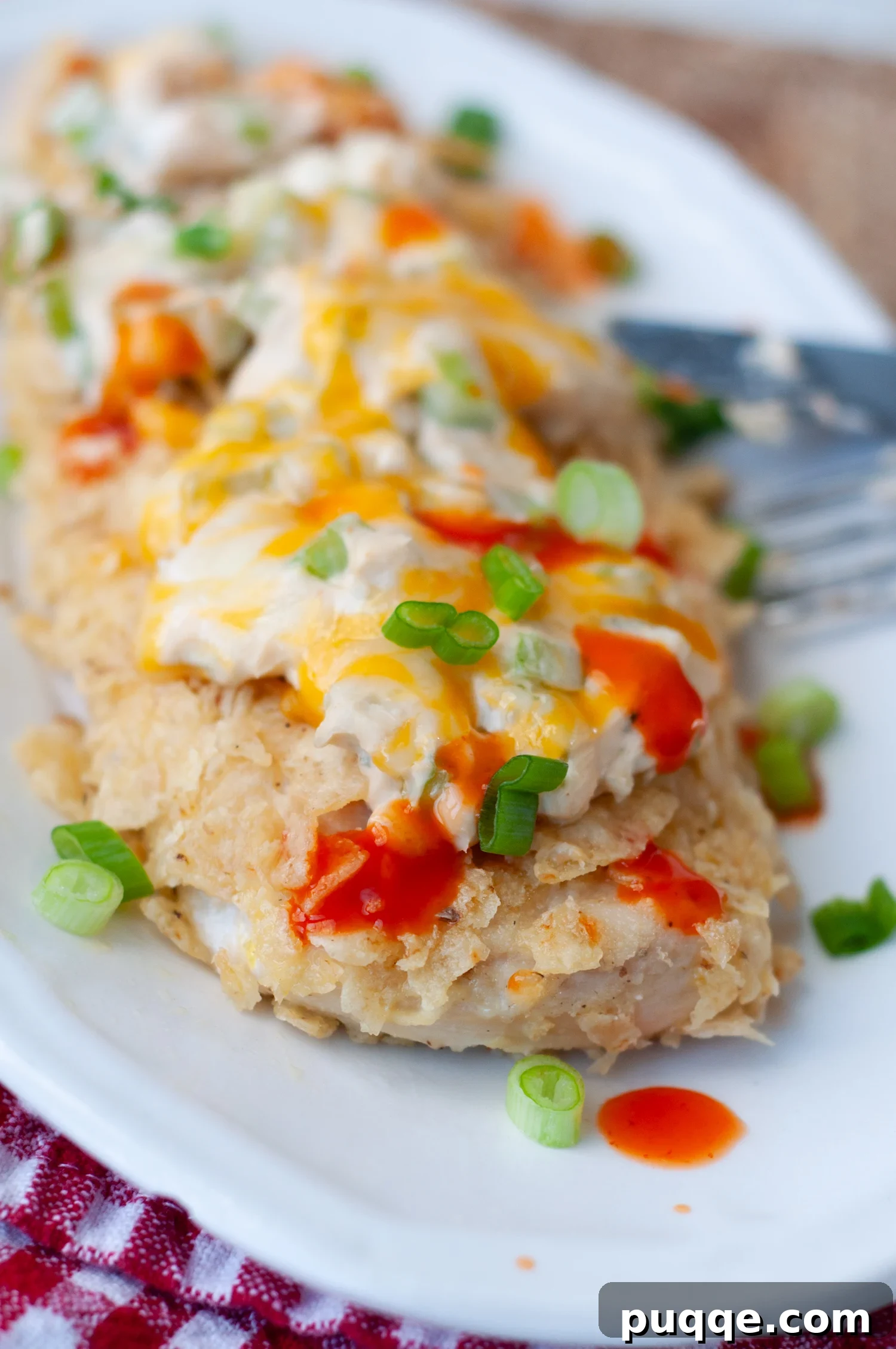 A serving of crispy, golden-brown tortilla crusted chicken with creamy buffalo sauce and melted cheddar cheese, drizzled with hot sauce.