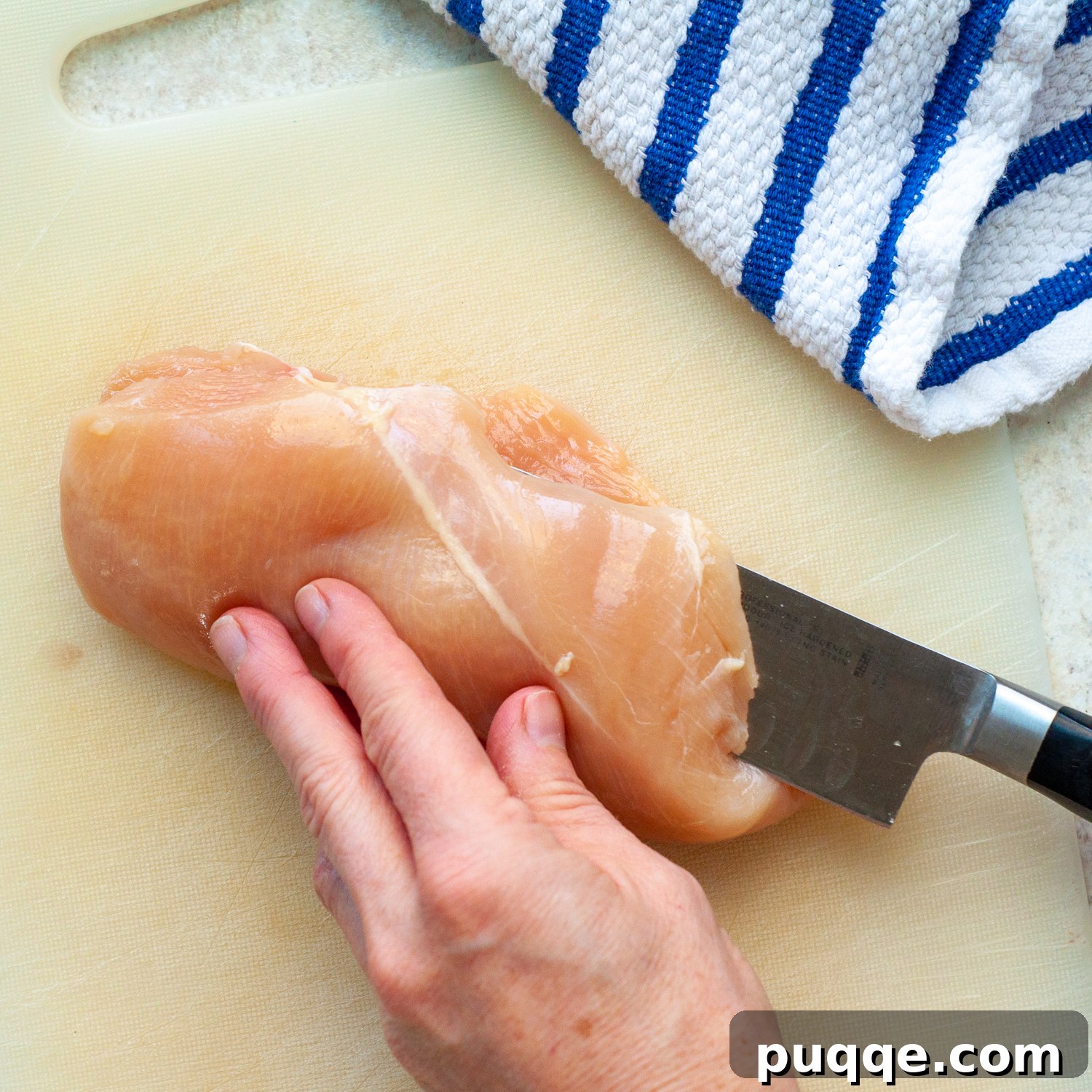 A knife slicing a chicken breast horizontally to create a thinner cutlet.