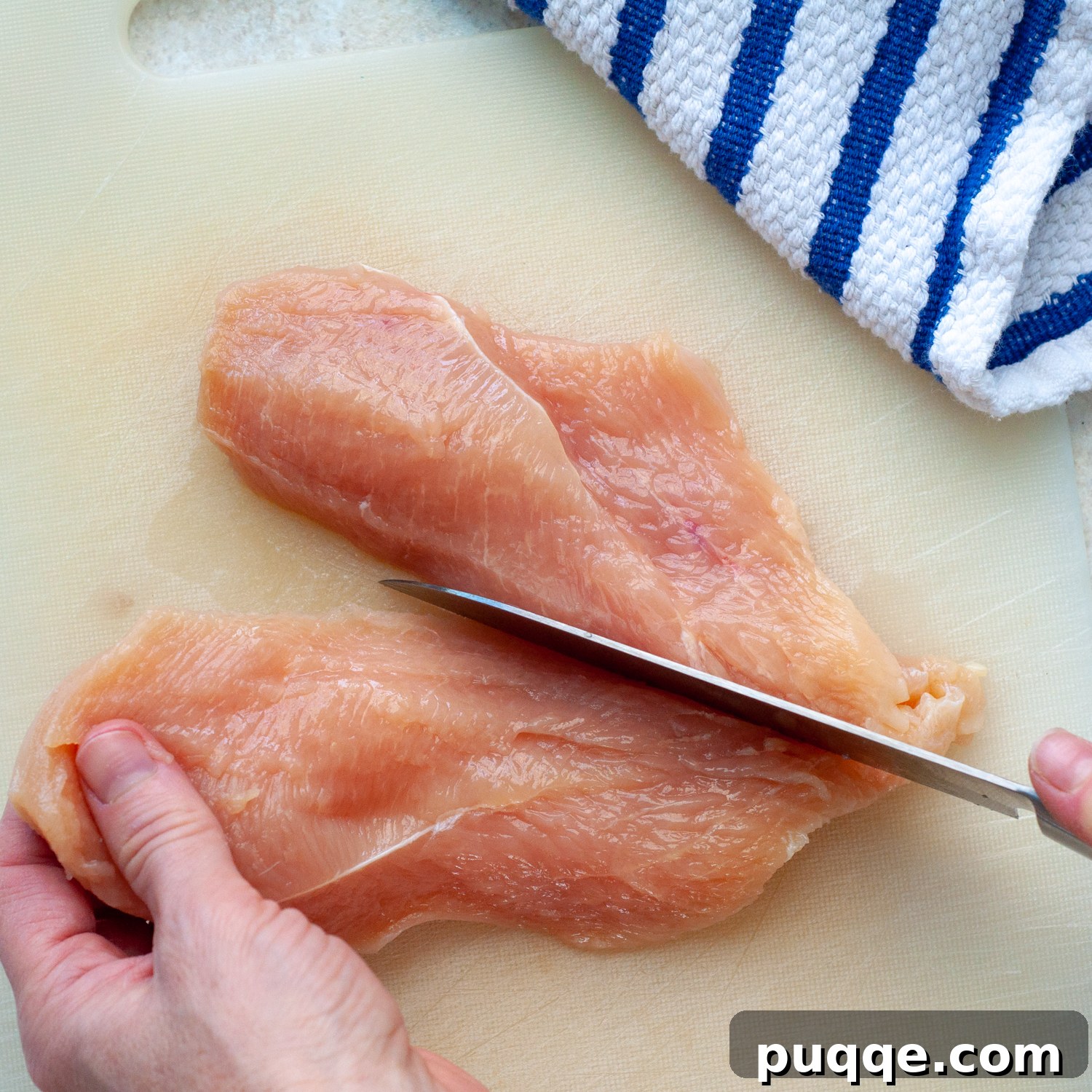 The butterflied chicken breast being cut into two equal, thinner cutlets.