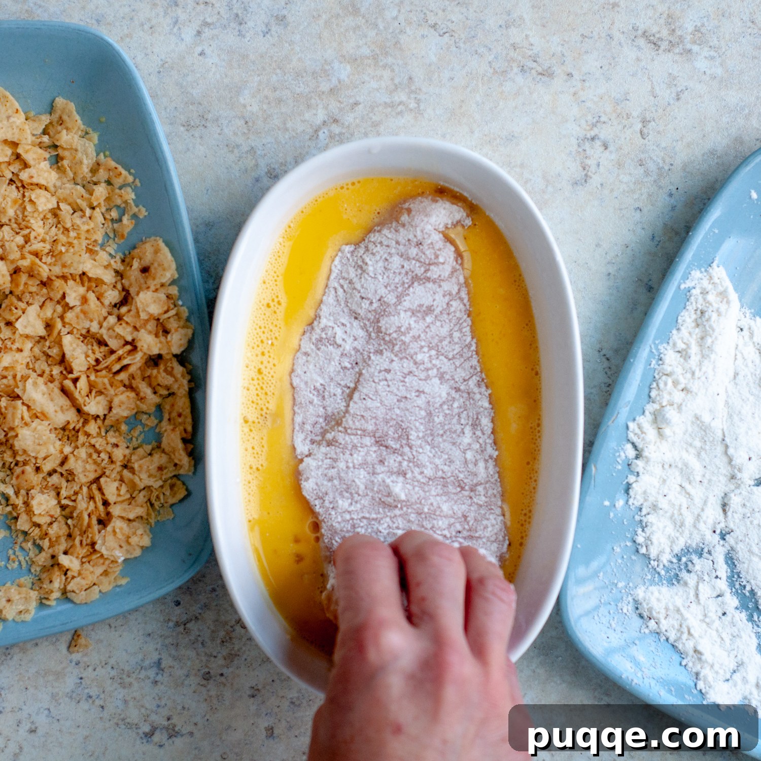Chicken cutlets being dredged in all-purpose flour before coating.