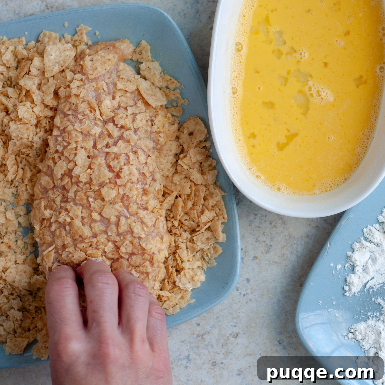 Chicken cutlets coated with crushed tortilla chips, ready for baking.