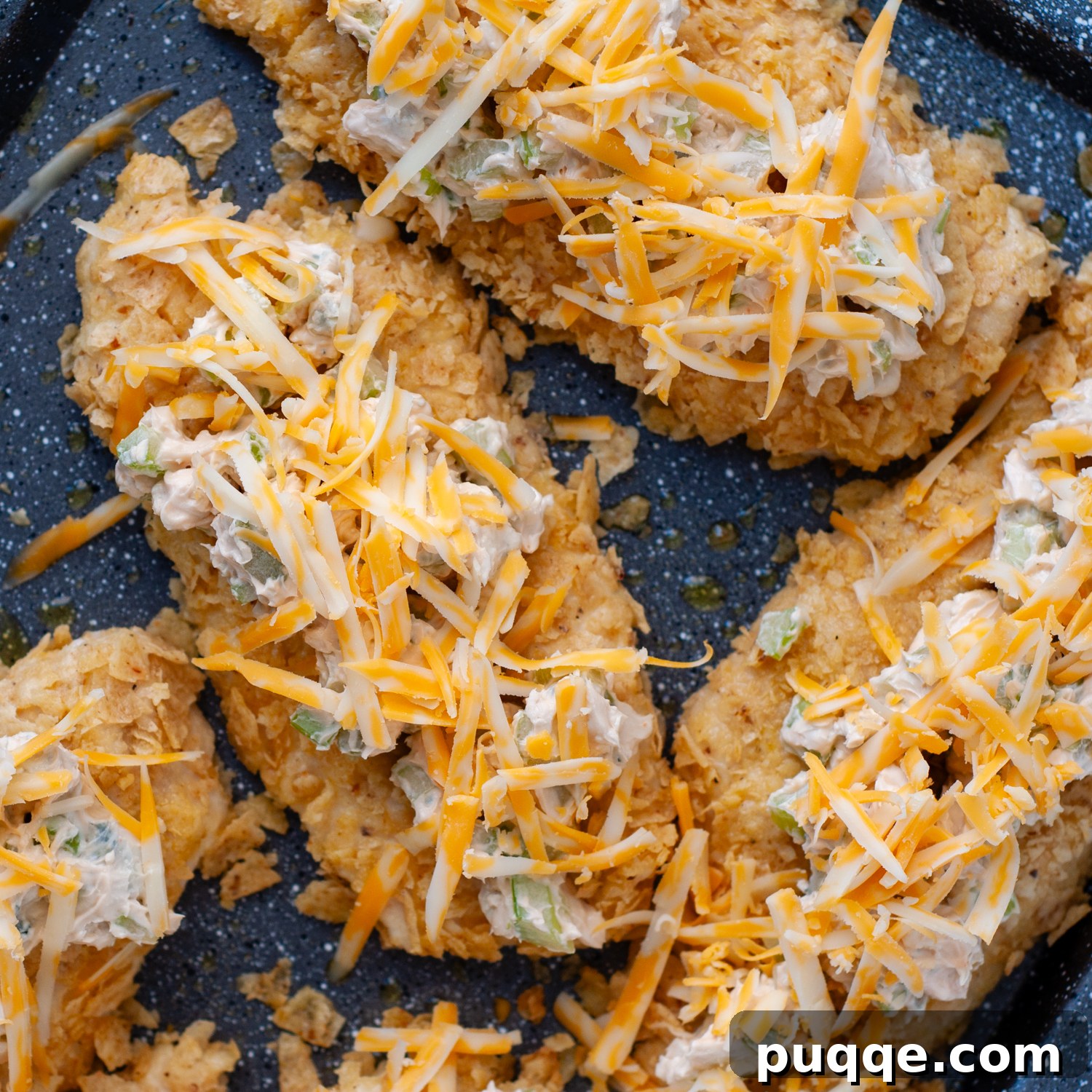 Shredded cheese sprinkled on top of chicken with buffalo topping before broiling.