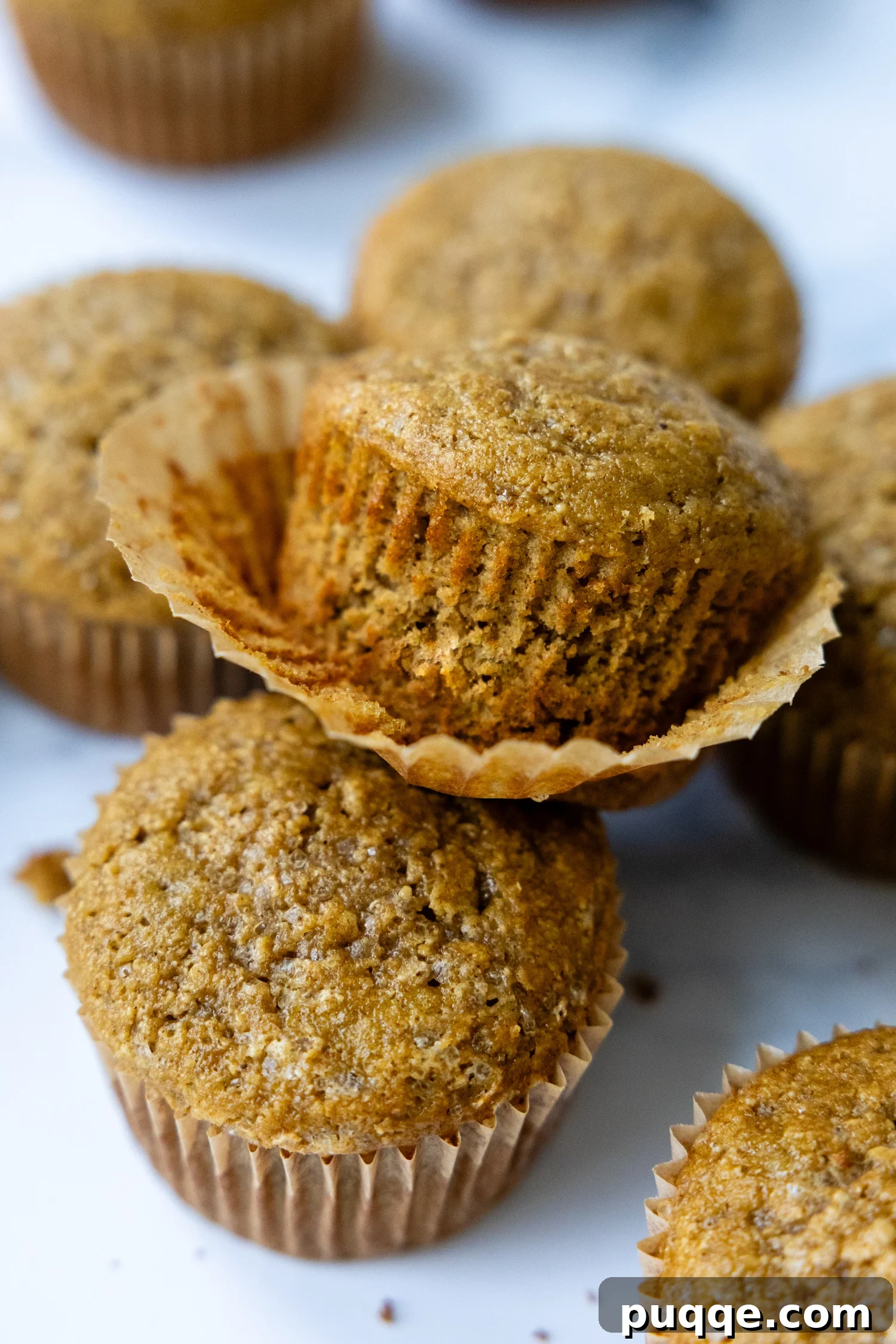 Pillowy Soft Gluten Free Oat Flour Banana Muffins 2 A stack of golden-brown banana oat muffins with a wrapper peeled back, revealing their fluffy texture.