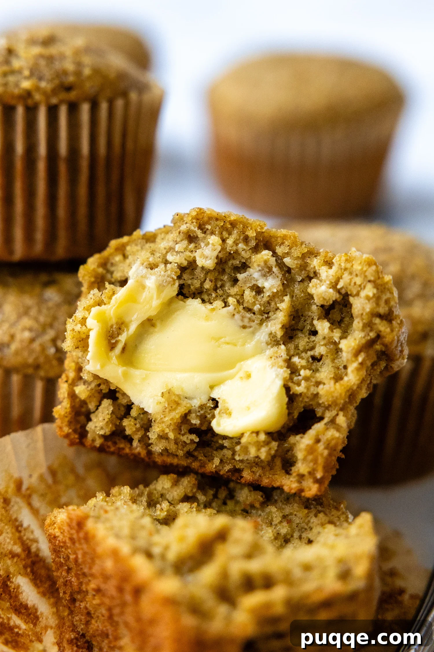 Pillowy Soft Gluten Free Oat Flour Banana Muffins 6 A freshly baked banana oat muffin cut open, with a dollop of butter spread on top, highlighting its soft interior.