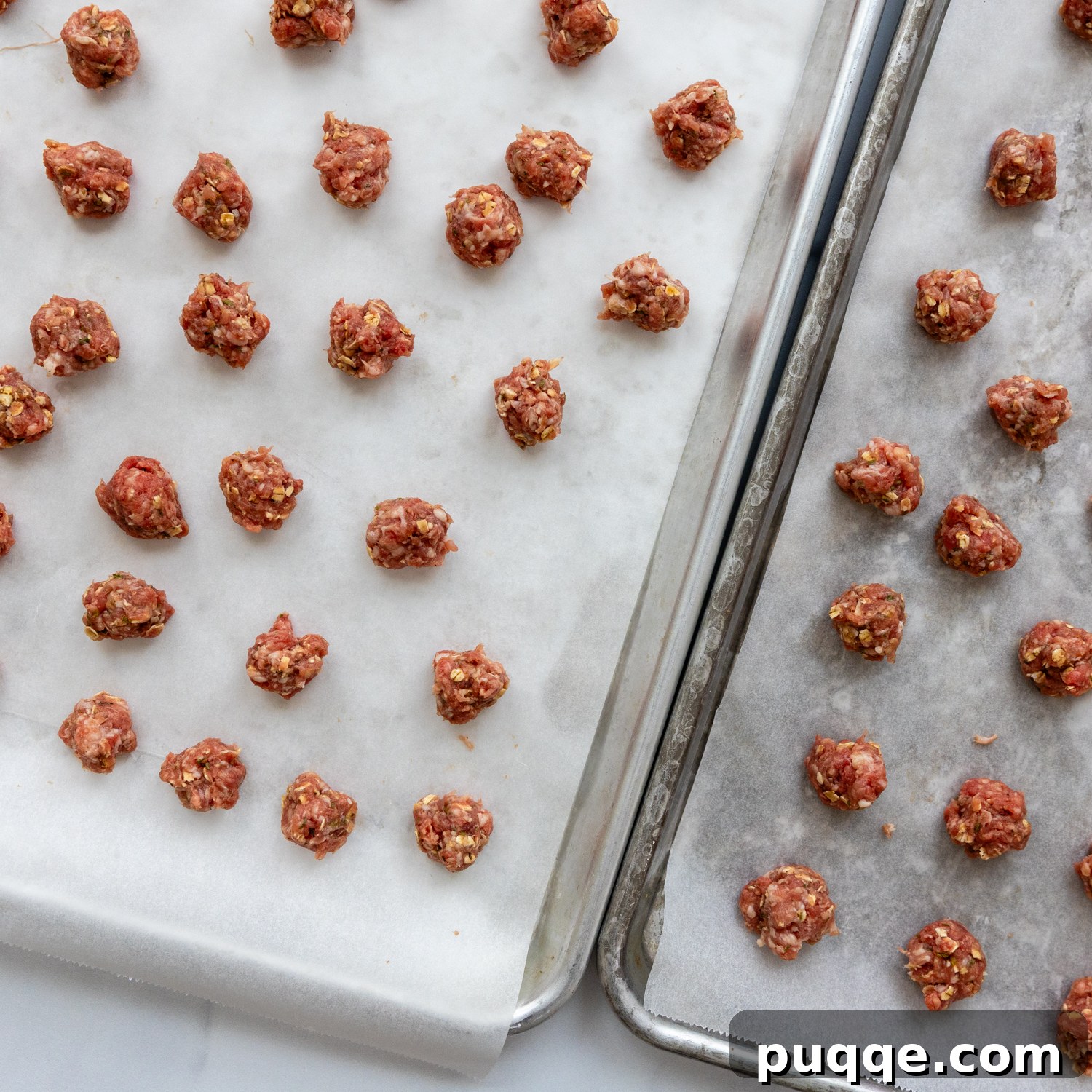 Raw meatballs evenly spaced on parchment paper on a baking sheet, ready for the oven.