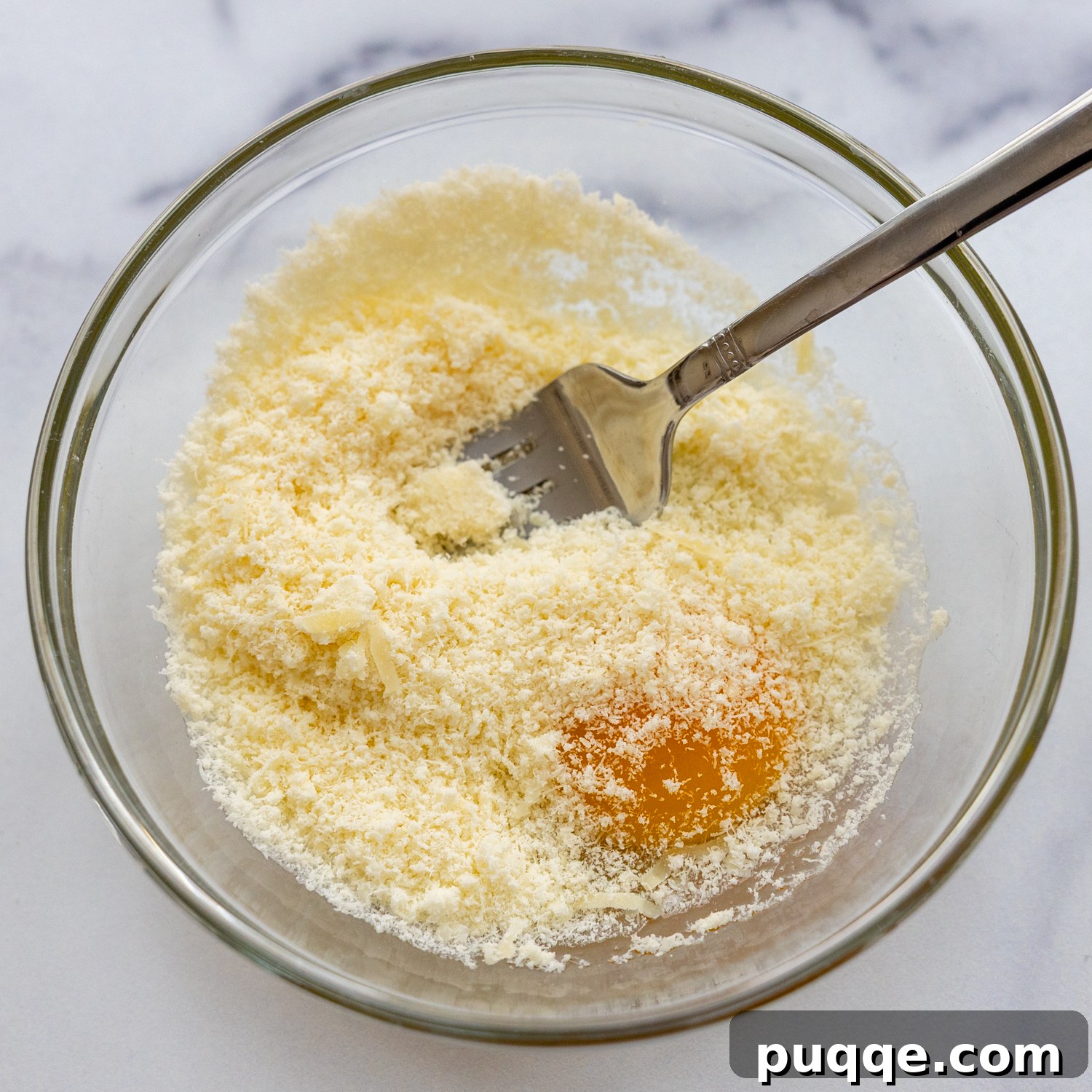 A small glass bowl containing a whisked egg and grated Parmesan cheese, ready to be added to the soup.