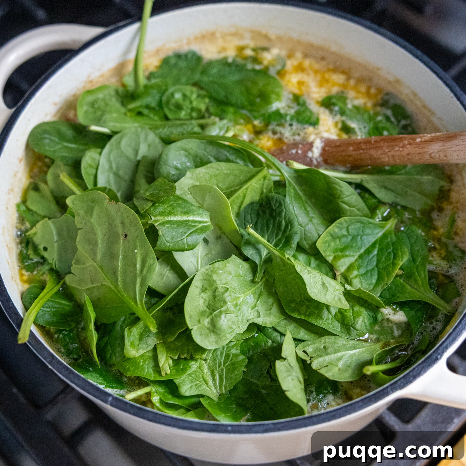 Fresh baby spinach being gently folded into a stockpot of Italian wedding soup ingredients.
