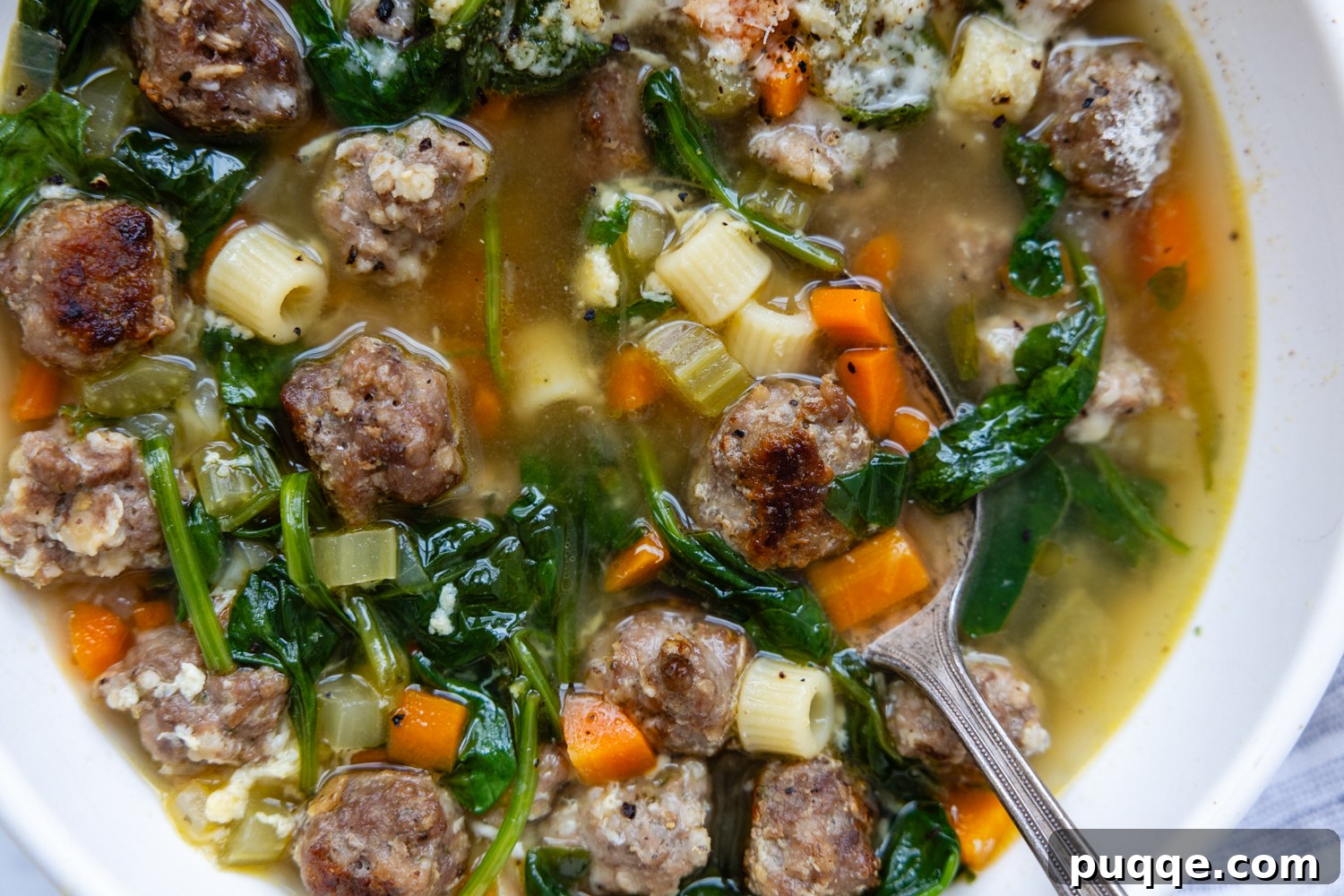A white bowl filled with steaming Gluten-Free Italian Wedding Soup, with a spoon resting in it.