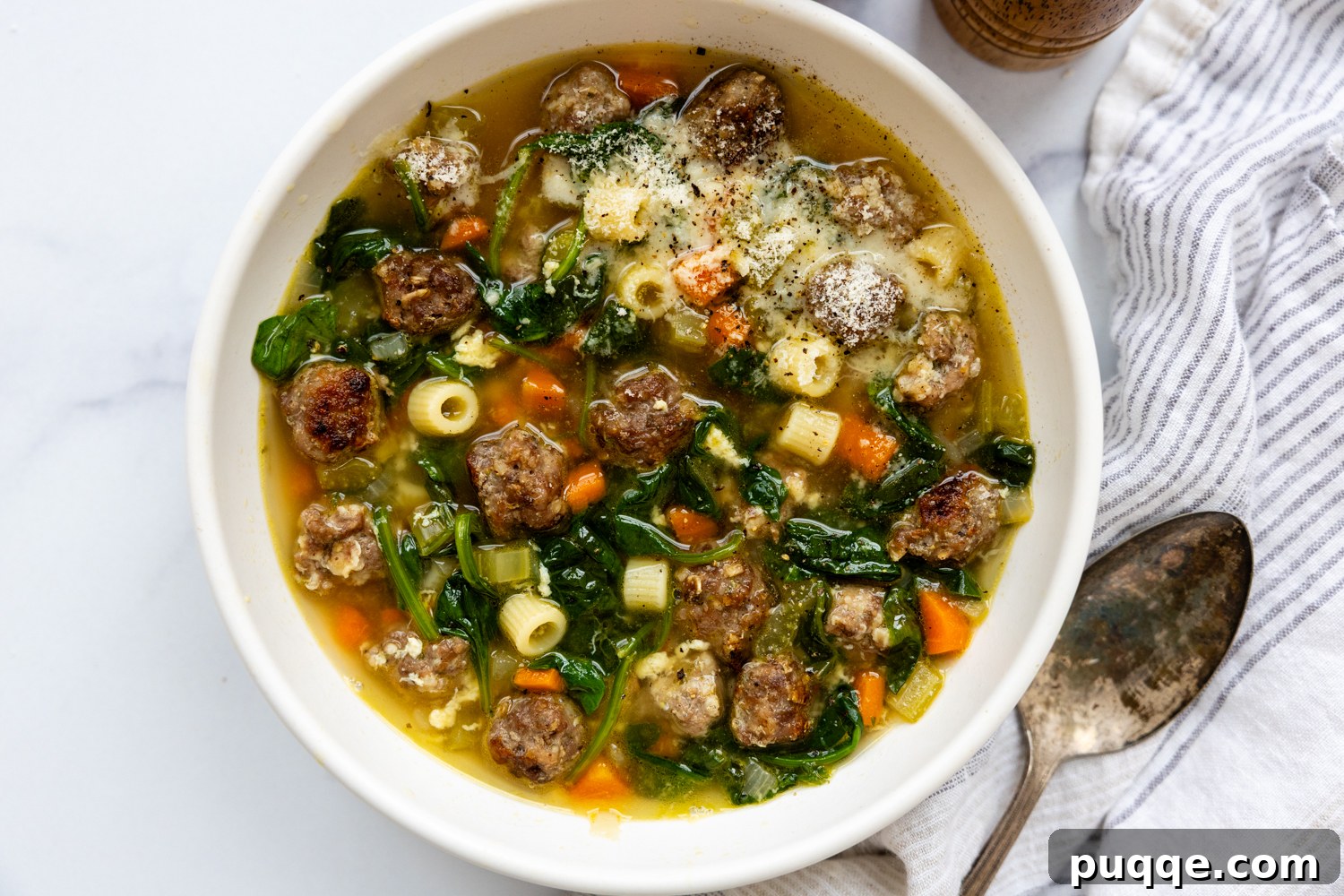 A pristine white bowl brimming with Gluten-Free Italian Wedding Soup, with a spoon neatly placed beside it on a light background.