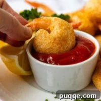 A hand dipping the crispy shrimp in a white dish of shrimp sauce.