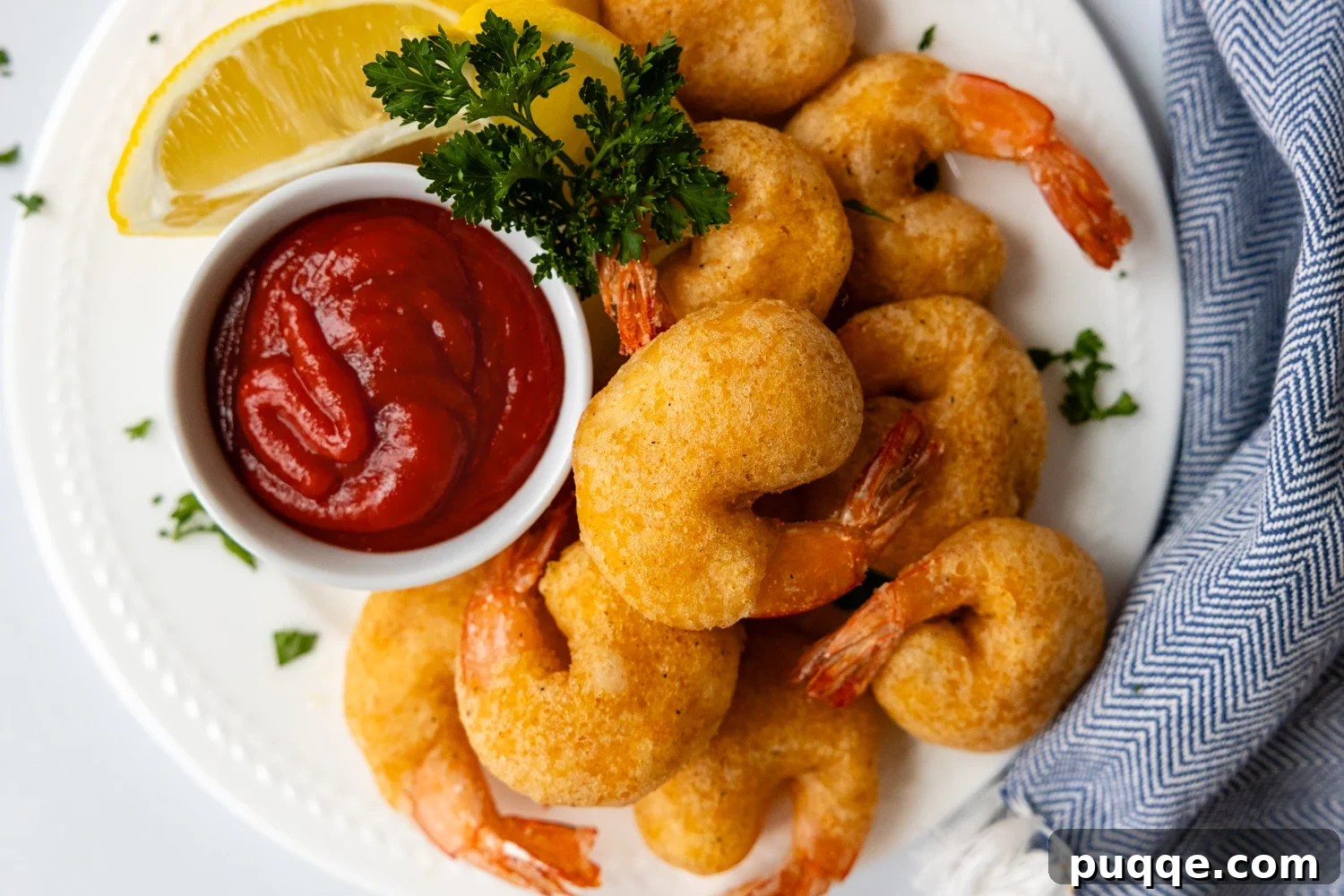 Golden Crispy Gluten-Free Shrimp 9 An overhead shot of a white plate piled with crispy golden fried shrimp, accompanied by a small dish of shrimp dipping sauce.