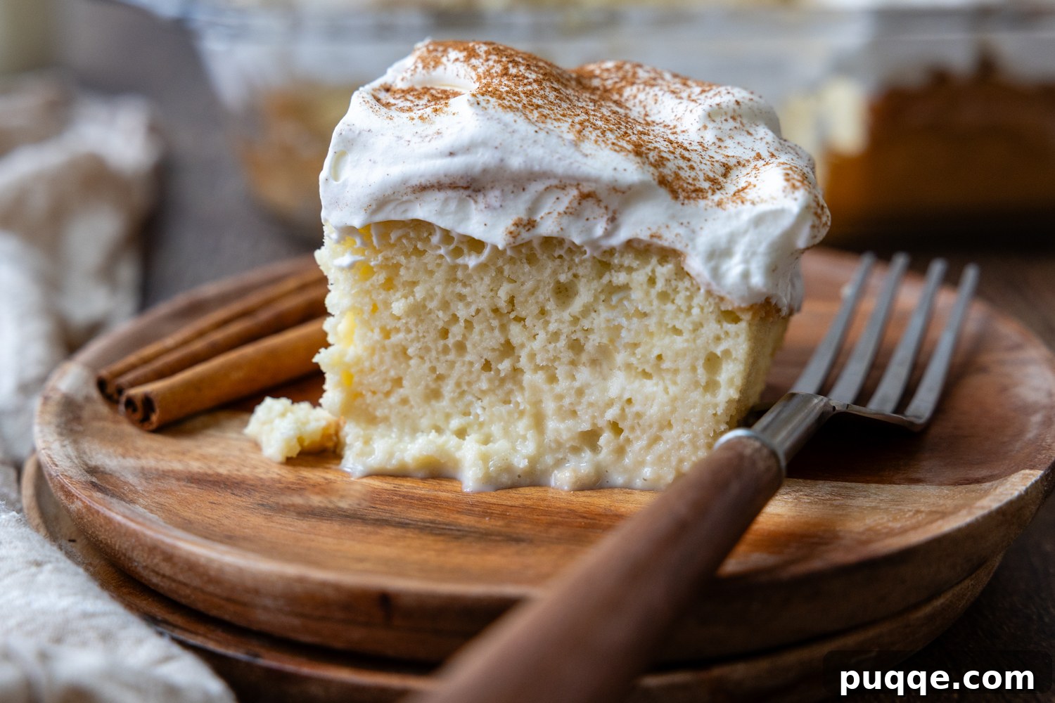 Absolutely Perfect Gluten-Free Tres Leches Cake 10 A delectable slice of gluten-free Tres Leches cake on a wooden plate, accompanied by a fork.