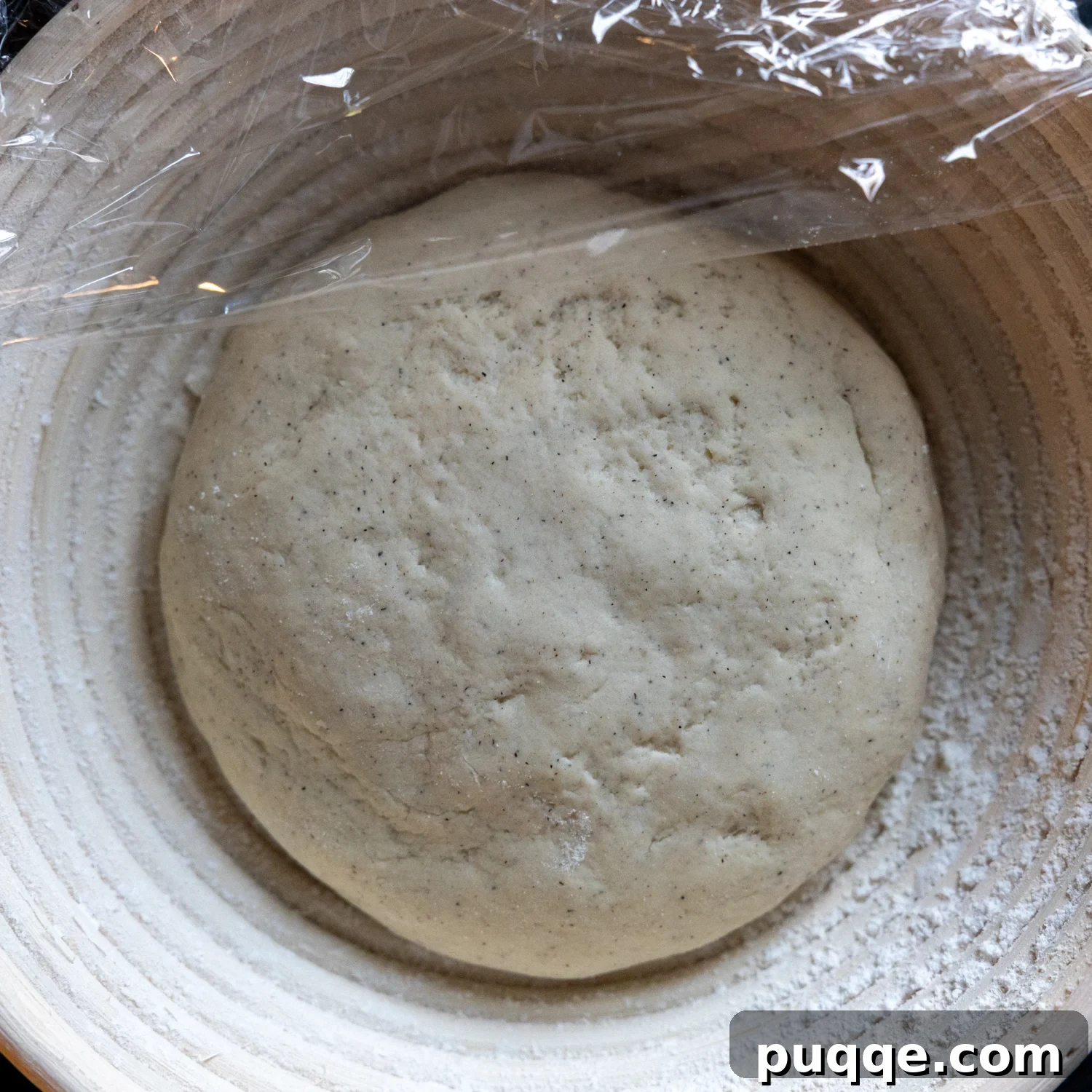 Gluten-free sourdough loaf covered with plastic wrap, proofing in a bowl for its cold rise.