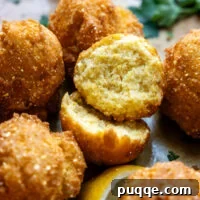 Cooked hush puppies with one cut in half showing inside texture.