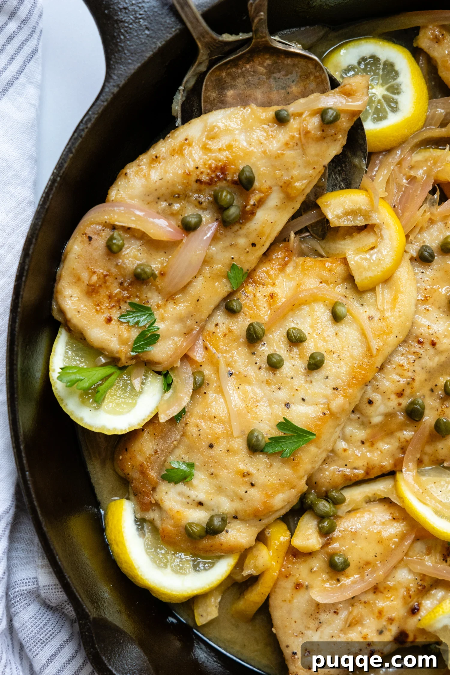 Gluten Free Chicken Piccata in a skillet with lemon garnish and topped with capers.