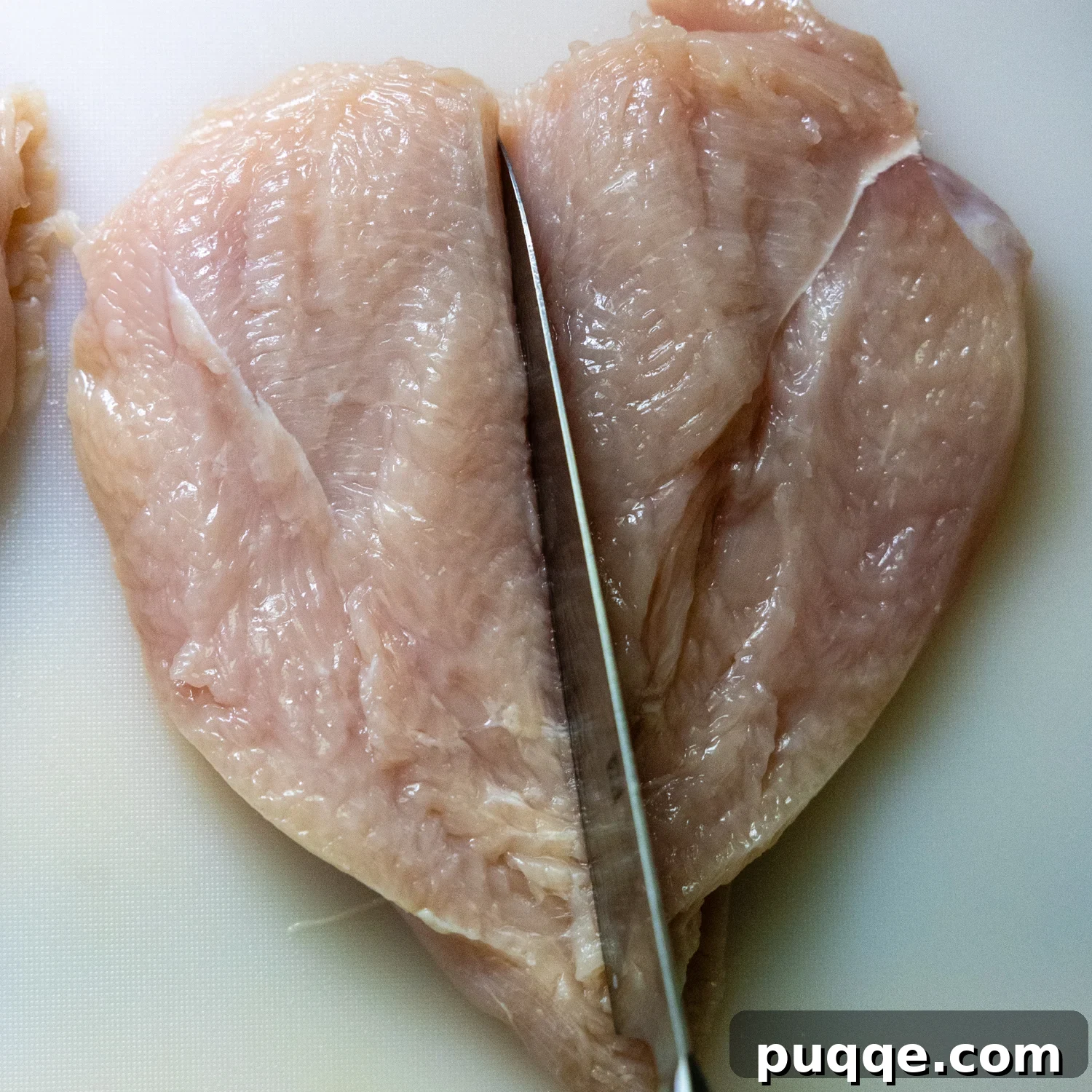 Raw chicken cutlet being cut in half.