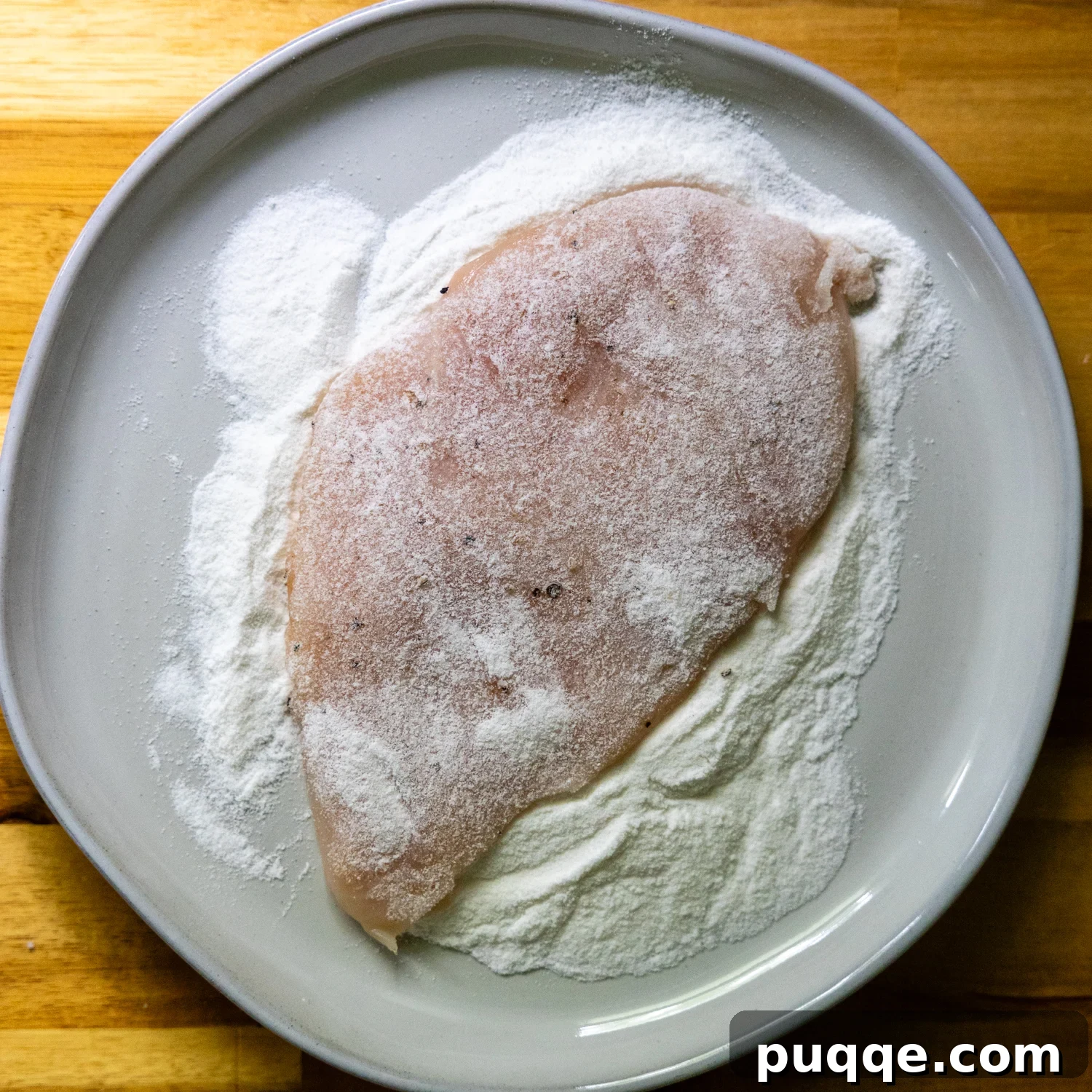 Chicken cutlet being dredged in rice flour.