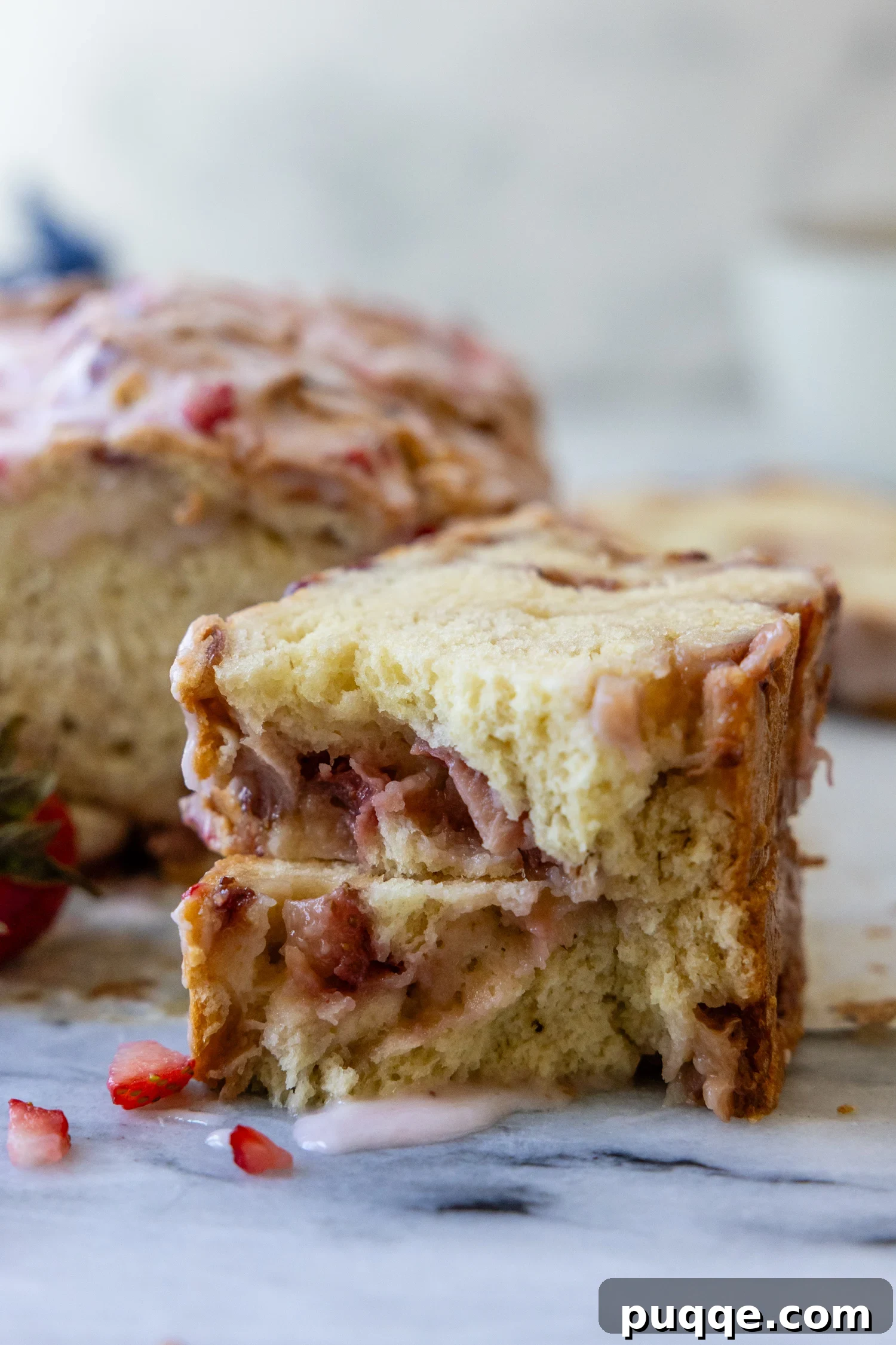 Gluten-Free Fresh Strawberry Quick Bread with Gooey Glaze 2 strawberry bread slice broken in half on a marble surface with glaze dripping down.