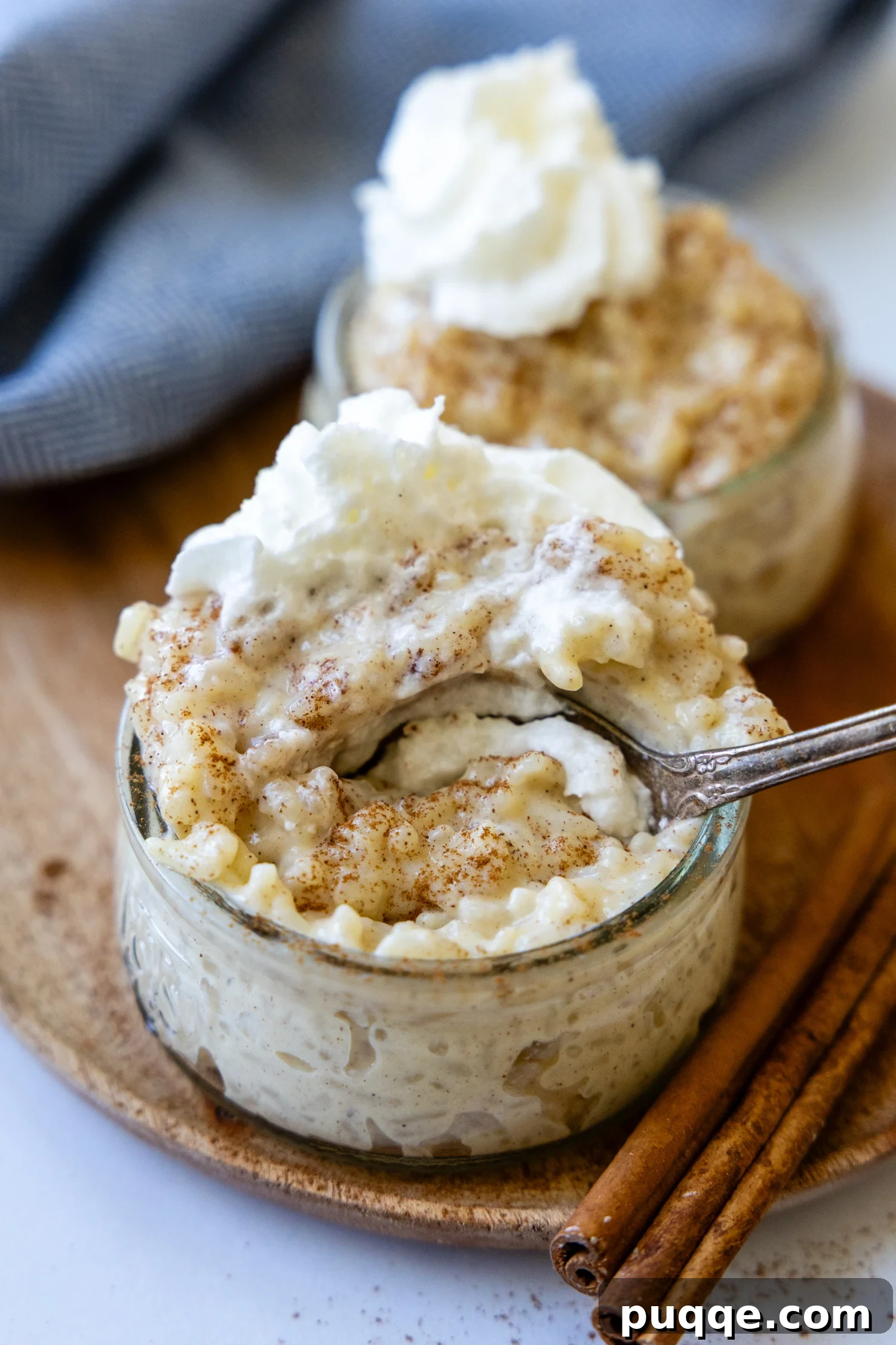 Microwave Rice Pudding for Two in 5 Minutes 2 a spoon going into a small glass bowl of rice pudding with whipped cream on top.