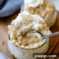 Microwave Rice Pudding for Two in 5 Minutes 3 a spoon going into a small glass bowl of rice pudding with whipped cream on top.
